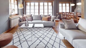 A modern living room with a sectional sofa, a coffee table, and a dining area with wooden chairs and a table. - El Jardi Secret by FeelFree Rentals (Escuñau)