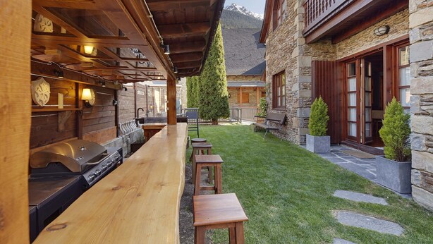 A wooden outdoor seating area with a grill, stone walls, and a mountain view. - El Jardi Secret by FeelFree Rentals (Escuñau)