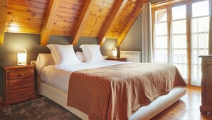A bedroom with a wooden ceiling, a large bed with white linens, two bedside tables with lamps, and a window with curtains. - El Jardi Secret by FeelFree Rentals (Escuñau)