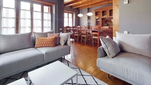 A modern living room with a grey sofa, white coffee table, and patterned cushions. A dining area with wooden chairs and a table is visible in the background. - El Jardi Secret by FeelFree Rentals (Escuñau)