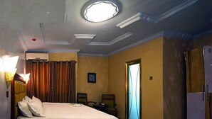 A hotel room with a bed, a nightstand, a lamp, a door, and a window. - Bleu Ivy Hotel & Suites (Lagos)
