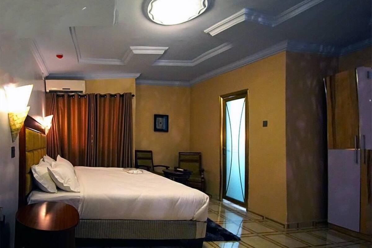 A hotel room with a bed, a nightstand, a lamp, a door, and a window.