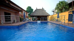 A swimming pool with a thatched-roof structure in the background. - Bleu Ivy Hotel & Suites (Lagos)