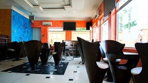 A modern interior with a tiled floor, dark wooden chairs, a flat-screen TV, and a large window. - Bleu Ivy Hotel & Suites (Lagos)