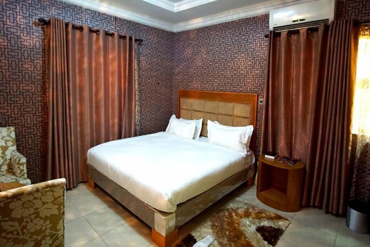 A hotel room with a large bed, patterned wallpaper, and curtains.