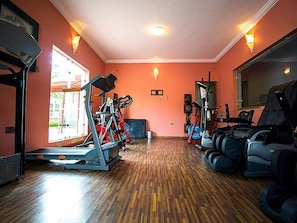 Un gimnasio con equipamiento de ejercicio, suelo de madera y amplios ventanales.