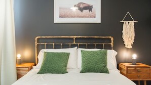 Ein ordentlich bezogenes Bett mit zwei grünen Kissen, ein gerahmtes Bild eines Bisons an der Wand und ein Wandbehang aus Makramee.