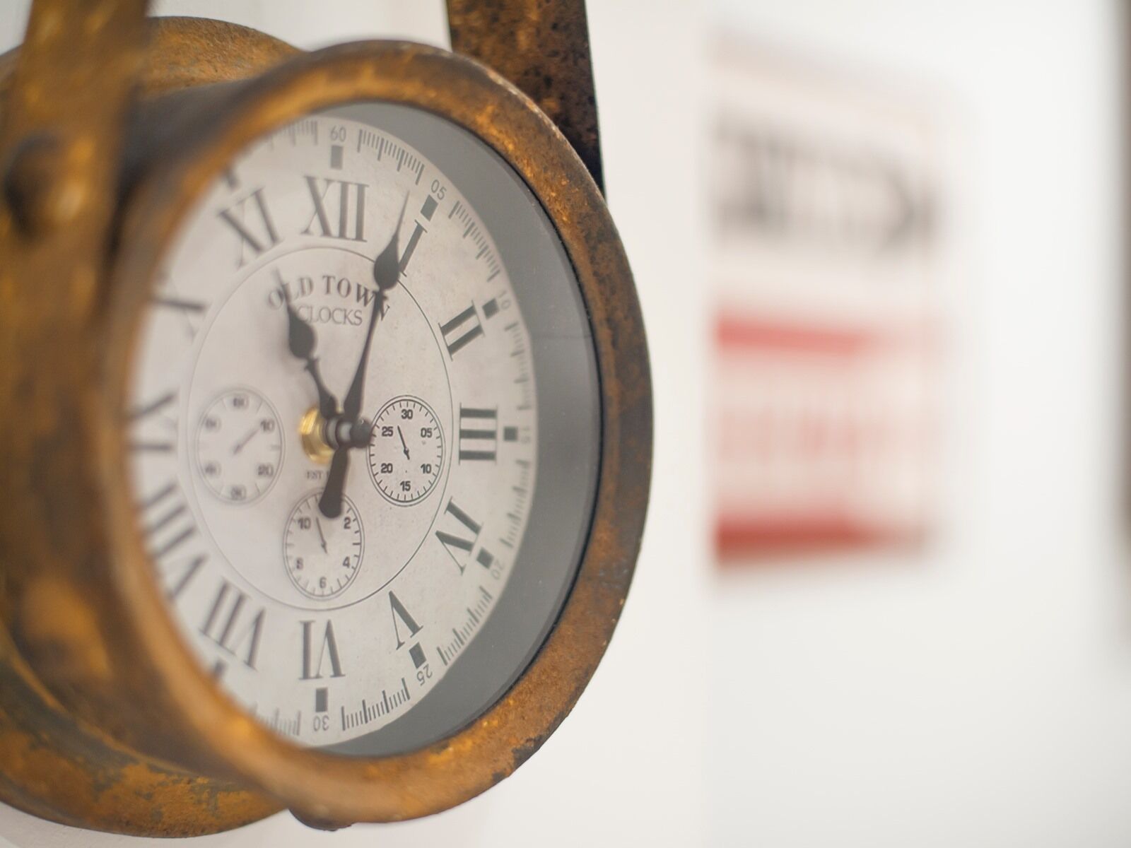 A close-up of a clock with Roman numerals and a pendulum, mounted on a wall.