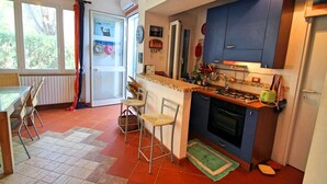 A compact kitchen with a stove, sink, and blue cabinets. There is a dining area with a table and chairs, and a window with curtains.