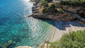 A coastal landscape with clear blue waters, rocky cliffs, and a paved walkway. - Three-Bedroom Seafront Villa, Brio Complex | Private Pool & Jetty | Sleeps 6–8 (Kefalonia Island)