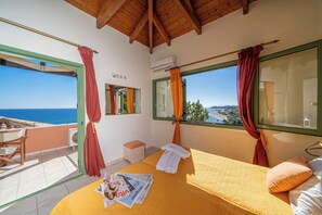 Une chambre avec un lit, une fenêtre avec des rideaux, une petite table avec une chaise et un appareil de climatisation.