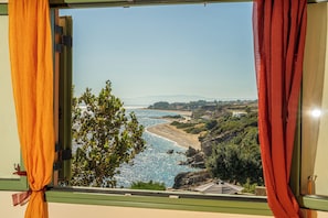 A window view of a coastal landscape with a clear sky, a beach, and greenery.