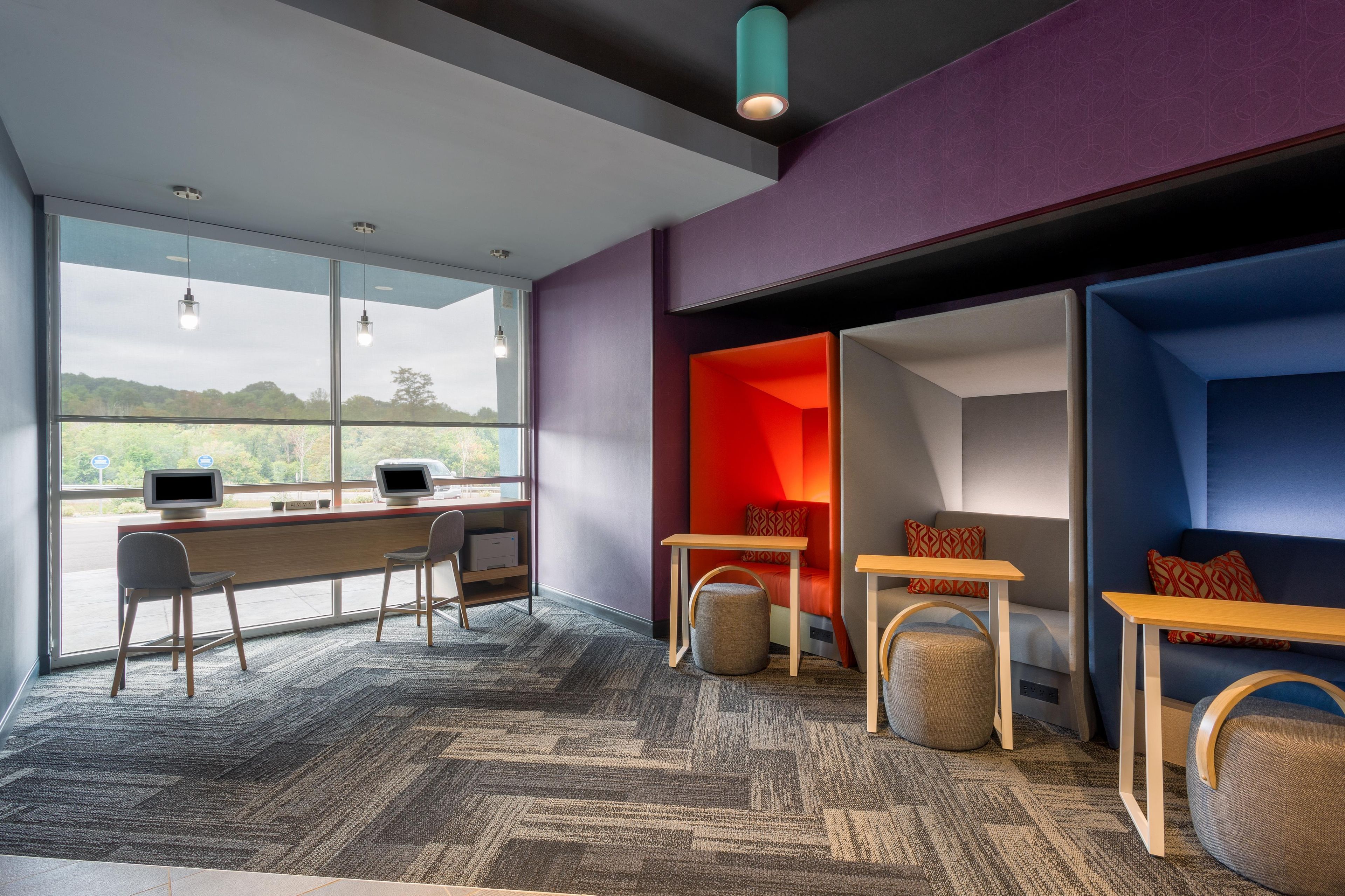 A modern office space with a large window, a desk with a computer, and a seating area with a red accent wall.