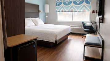 A modern hotel room with a bed, desk, chair, and a TV.