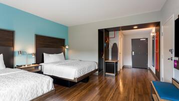 Habitación de hotel con dos camas, piso de madera y vista al pasillo.