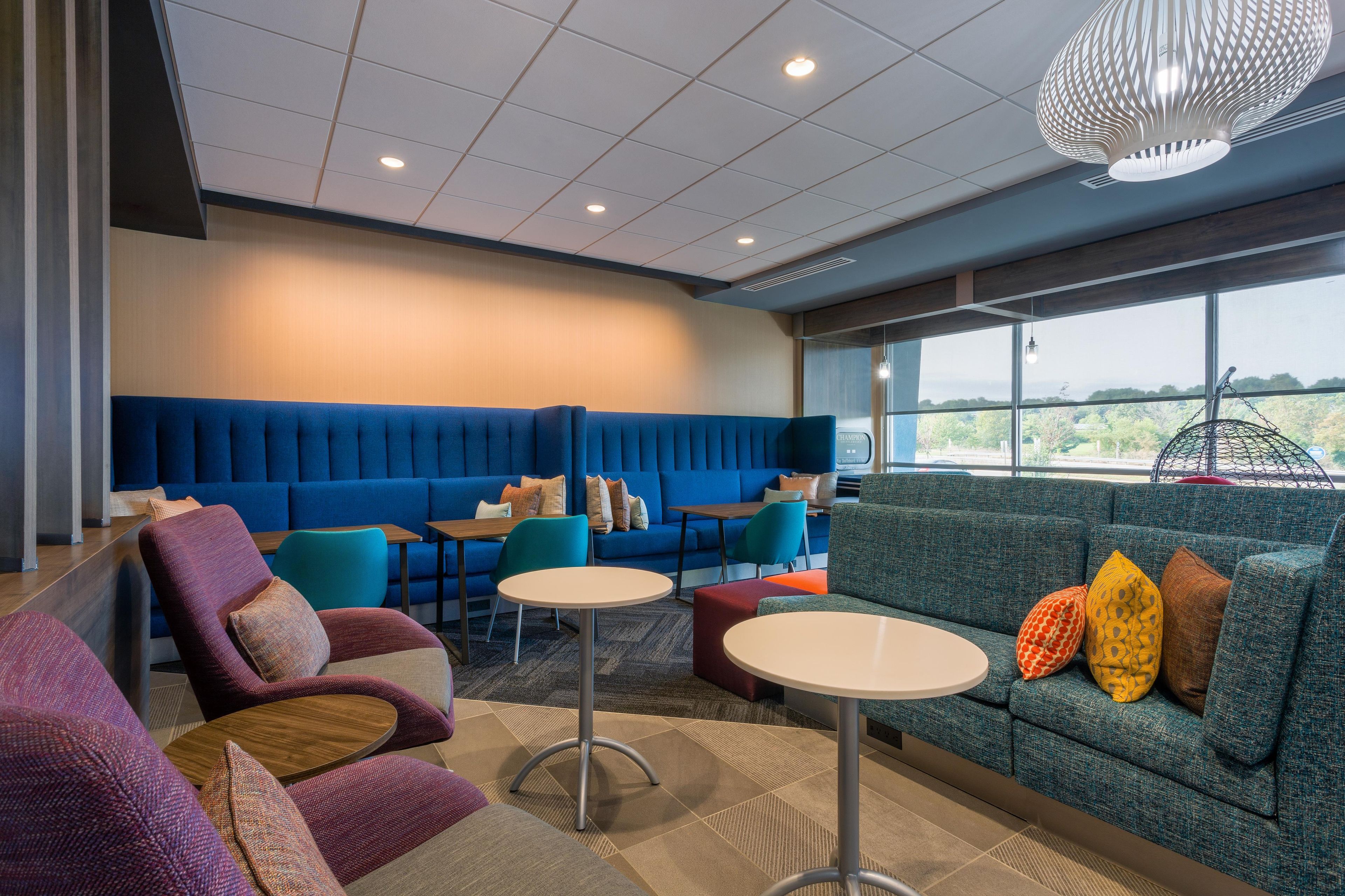 A modern lounge area with seating arrangements, a view through large windows, and a ceiling with recessed lighting.