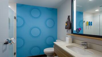 A bathroom with a blue patterned wall, a white toilet, a sink with a mirror, and a towel rack with a bag.