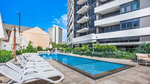 A swimming pool with lounge chairs, surrounded by greenery and modern buildings. - Surfers Paradise 2-Bed Near Beach with Pool & Gym (Surfers Paradise)