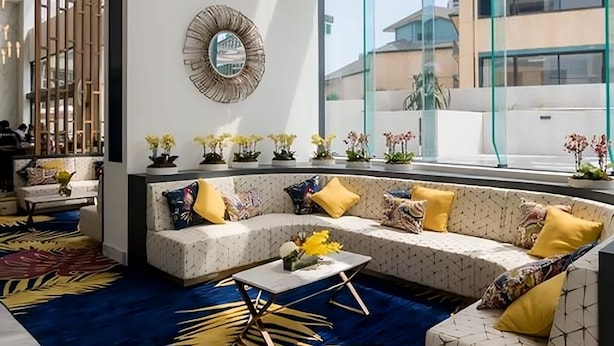 A modern hotel lobby with a large window, a sofa with yellow cushions, and a decorative mirror on the wall. - Surfers Paradise 2-Bed Near Beach with Pool & Gym (Surfers Paradise)