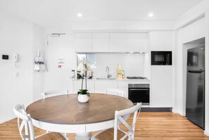 Une cuisine moderne avec des meubles blancs, une table de salle à manger ronde en bois et un four encastré.