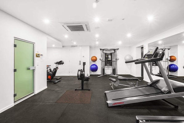 Une salle de sport équipée de tapis de course, d’appareils de musculation et de ballons d’exercice.
