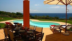 Un espace aménagé au bord de la piscine, avec une table dressée pour les repas, des chaises longues et une pergola dotée d’un parasol.