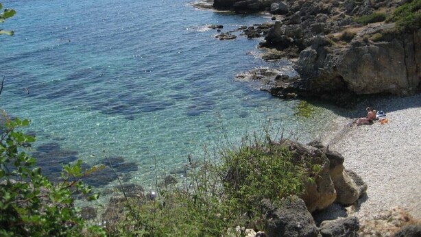 Une côte rocheuse bordée d’une eau d’un bleu limpide et d’une plage de sable.