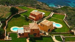 Une propriété située sur la côte, comprenant deux bâtiments principaux, une piscine et un jardin aménagé.