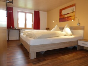 Quarto com cama de madeira, escrivaninha, cadeira, mesa de cabeceira e um quadro na parede.
