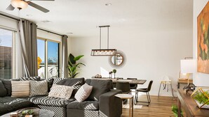A modern living room with a sectional sofa, a round coffee table, and a dining area with a wooden table and chairs. - CORAL CACTUS RETREAT- *DOG-FRIENDLY* Private oversized hot tub and ping pong! (Washington)