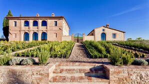 Un vignoble avec un sentier en pierre menant à un bâtiment doté de nombreuses fenêtres en arc et d’une entrée fermée par un portail.