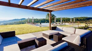 Un espace extérieur aménagé, abrité et doté de mobilier en osier, offrant une vue sur une piscine et des montagnes.