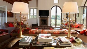 Un salon chaleureux avec une cheminée, deux canapés avec des coussins rouges et une table basse agrémentée de livres et d’objets décoratifs.