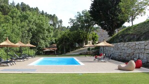 A swimming pool with lounge chairs and umbrellas, surrounded by a stone wall and trees. - Casa Moinho da Mouta (Sabrosa)