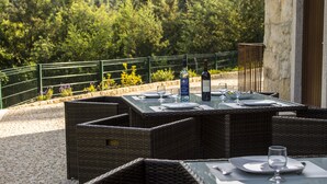 An outdoor dining area with wicker furniture and glass tables, set against a backdrop of lush greenery and a stone building. - Casa Moinho da Mouta (Sabrosa)