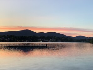 A calm lake with a dock, surrounded by mountains and a town in the background.