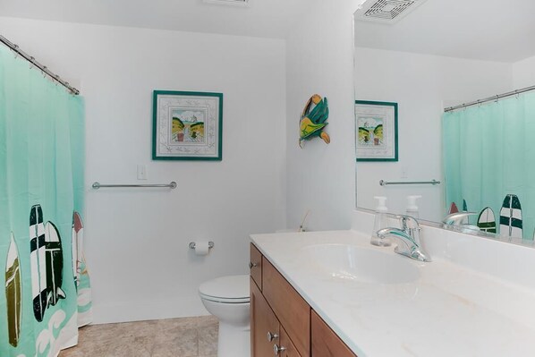 A bathroom with a white sink, a mirror, a toilet, and a shower curtain with a surfboard design. - SC202 Coastal LegaSea by First Flight Rentals (Kill Devil Hills)