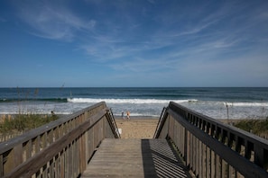 A wooden boardwalk leading to a beach with waves and a clear sky. - SC202 Coastal LegaSea by First Flight Rentals (Kill Devil Hills)