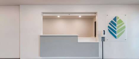A reception area with a light-colored desk, a wall-mounted artwork, and a floor lamp.