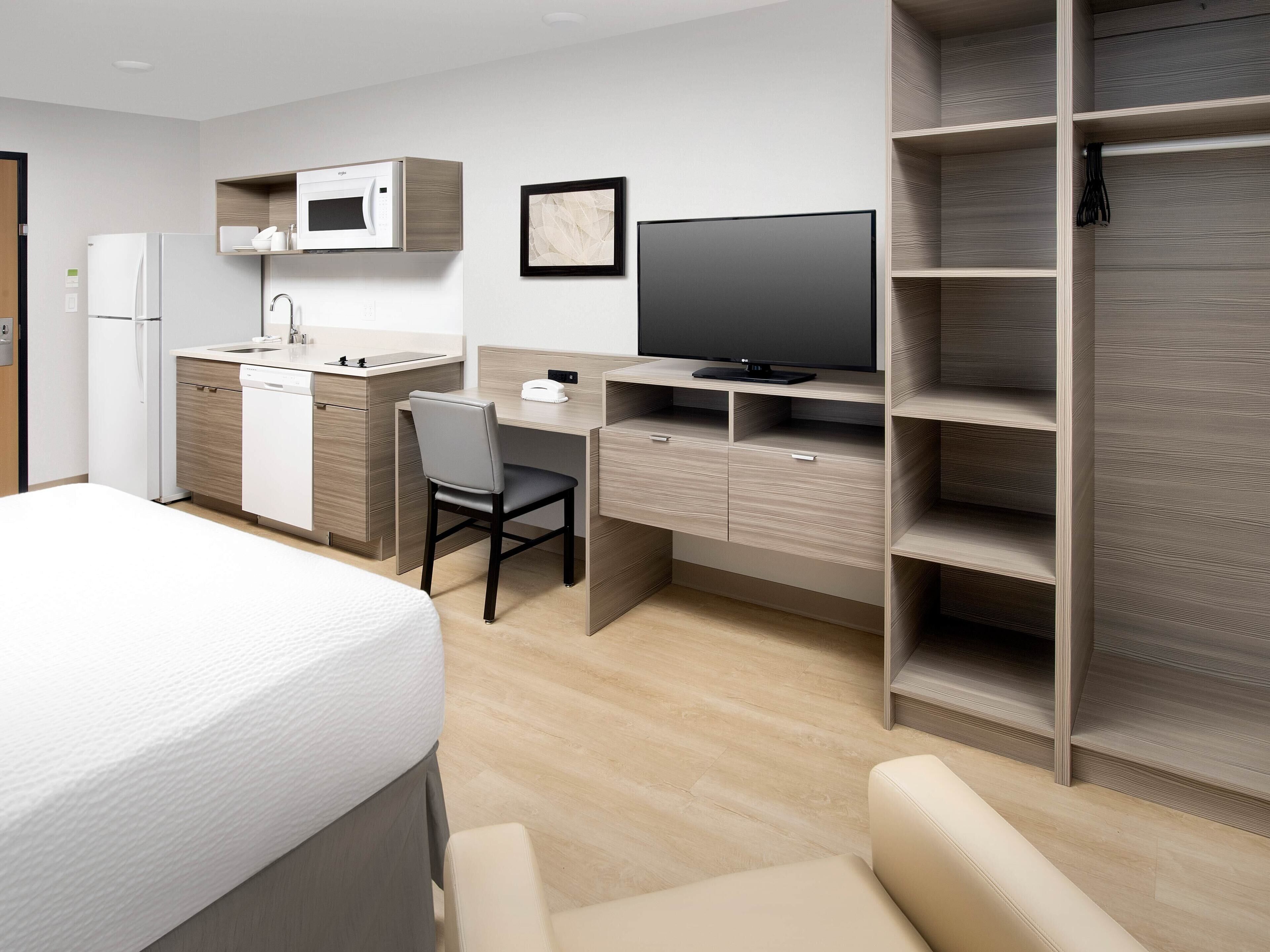 A compact hotel room with a bed, a desk with a chair, a television, a microwave, and a wardrobe.