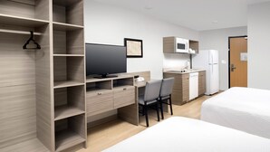 A hotel room with a wooden wardrobe, a desk with a chair, a bed, a television, a microwave, and a refrigerator. - WoodSpring Suites Tri-Cities - Richland  (Richland)
