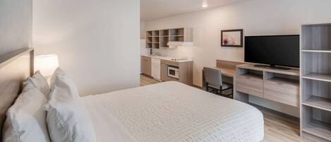 A modern hotel room with a large bed, a desk, a television, and built-in shelving.