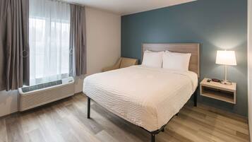 A hotel room with a bed, a nightstand, a lamp, and a window with curtains.
