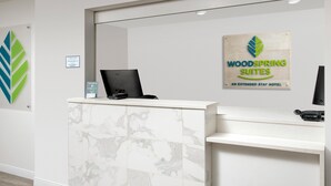 A reception desk with a laptop, a sign for Woodspring Suites, and a marble-patterned cabinet. - WoodSpring Suites Tri-Cities - Richland  (Richland)