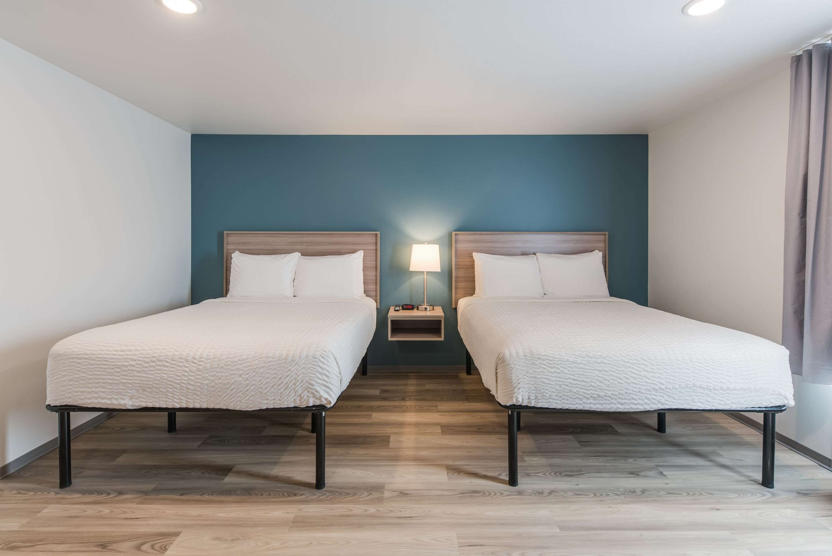 A hotel room with two single beds, a nightstand with a lamp, and a wooden floor.