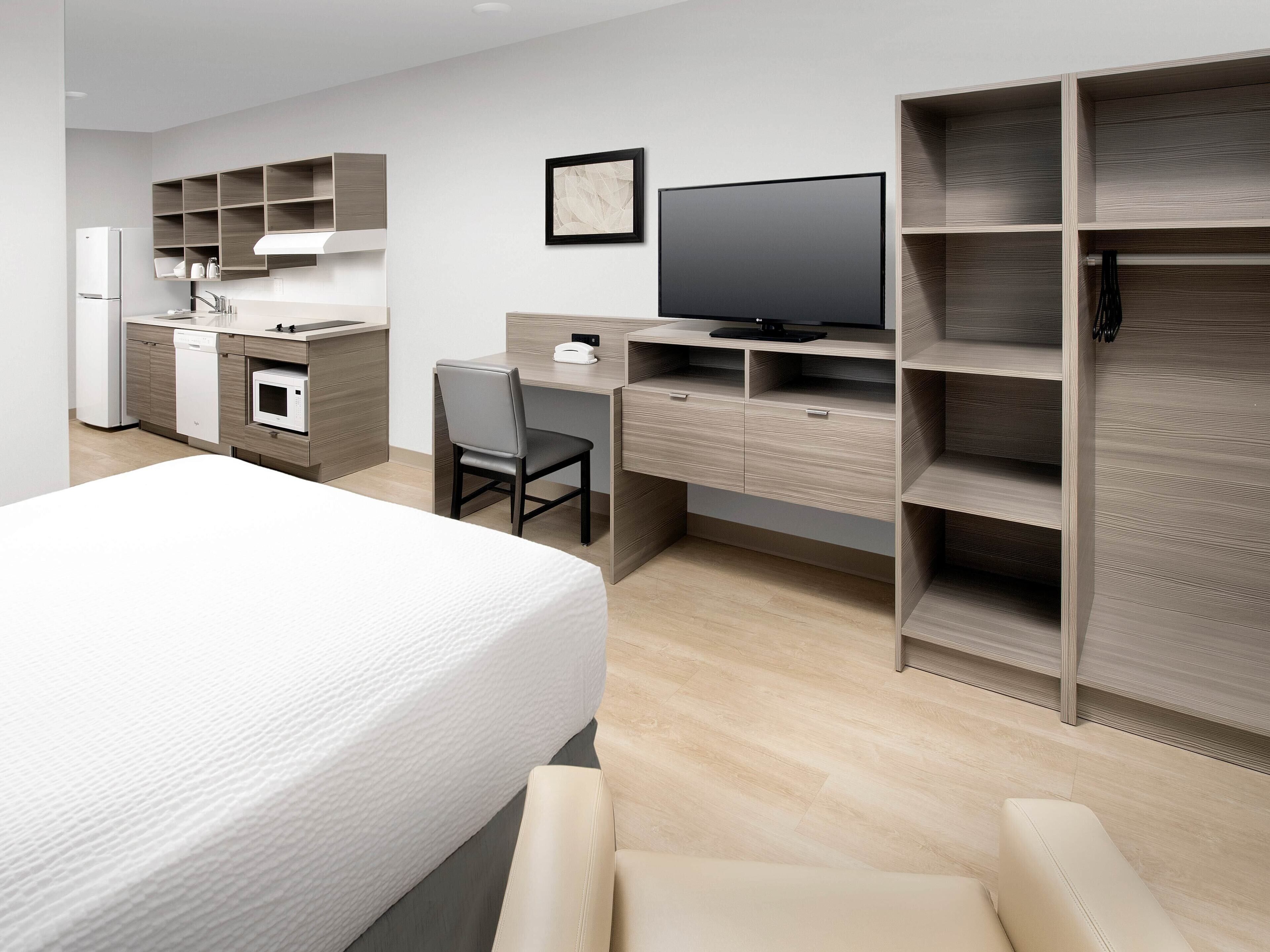 Una habitación de hotel moderna con cama, escritorio con silla, televisor y estanterías empotradas.