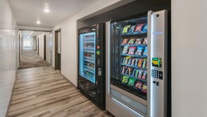 A hallway with a vending machine and a refrigerator stocked with beverages and snacks. - WoodSpring Suites Tri-Cities - Richland  (Richland)