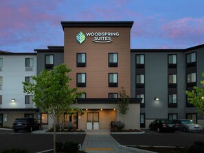 Un hotel de varios pisos con un llamativo letrero que dice "WOODS SPRING SUITES", que presenta un diseño moderno con una combinación de fachada de ladrillo y paneles.