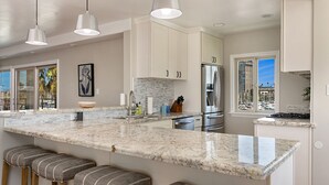 A modern kitchen with a large island, stainless steel appliances, and a view of the city. - Oceanfront dining, shopping, Pool, spa, and sauna on site!- The Harbor Penthouse (Oceanside)
