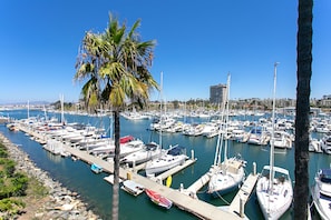 A marina with numerous boats docked, a palm tree, and a clear blue sky. - Oceanfront dining, shopping, Pool, spa, and sauna on site!- The Harbor Penthouse (Oceanside)